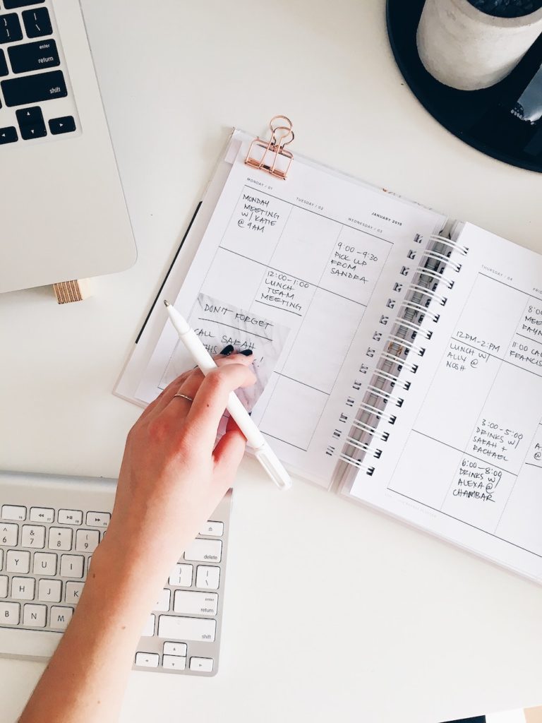 Freelance writer with full planner and a busy schedule, updating her calendar on her desk, near her keyboard.